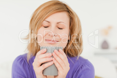 Prety red-haired woman holding and smelling a cup of coffee whil