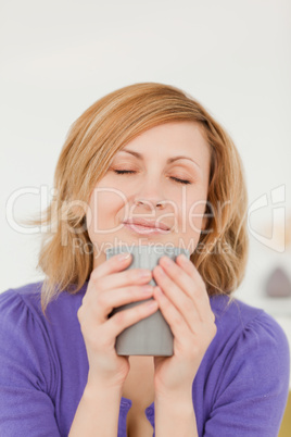 Attractive red-haired woman holding and smelling a cup of coffee