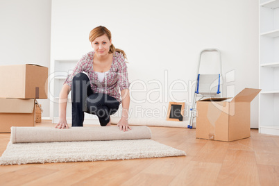 Pretty blonde woman rolling up a carpet to prepare to move house
