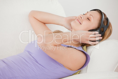Serene blond-haired woman listening to music lying on the sofa