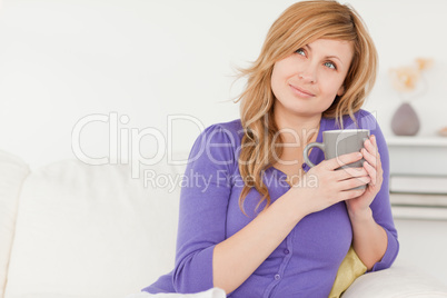 Pretty red-haired woman holding a cup of coffee while sitting on