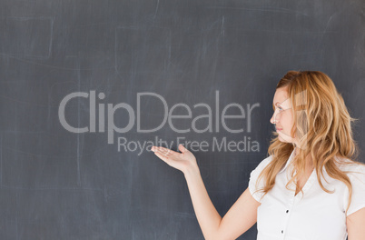 Attractive teacher showing an empty blackboard
