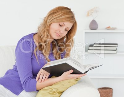 Pretty red-haired woman reading a book while sitting on a sofa