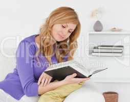Pretty red-haired woman reading a book while sitting on a sofa