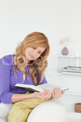 Beautiful red-haired woman reading a book sitting on a sofa
