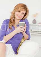 Good looking red-haired woman holding a cup of coffee while sitt