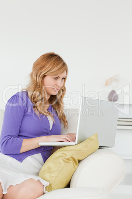 Prettyl red-haired woman sitting on the sofa and using a laptop