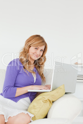 Attractive red-haired woman sitting on the sofa and using a lapt