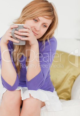 Pensive red-haired woman holding a cup of coffee while sitting o