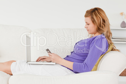 Beautiful red-haired woman using a laptop and phone while lying