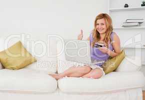 Glad woman sitting on a sofa is going to make a payment on the i