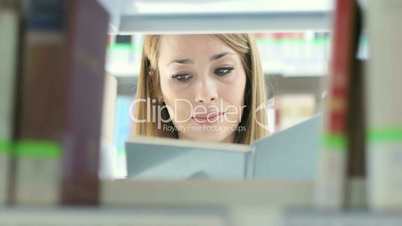 Attractive young woman choosing book on shelf in library