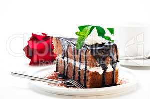 A piece of chocolate cake with vanilla cream and a rose