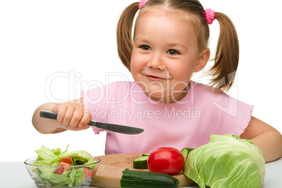 Little girl is cutting carrot for salad