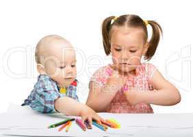 Two children are drawing on paper using markers