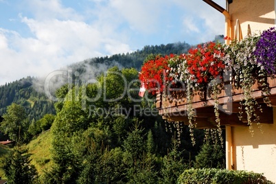 Alpine chalet balcony with flowers on green hills background