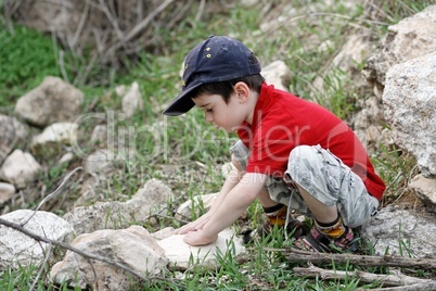 Little boy squatting on stones outdoors