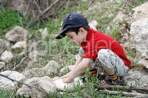 Little boy squatting on stones outdoors