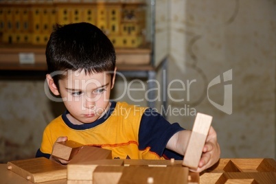 Cute little boy plays with wooden bricks indoors and builds a house