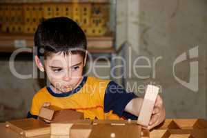 Cute little boy plays with wooden bricks indoors and builds a house