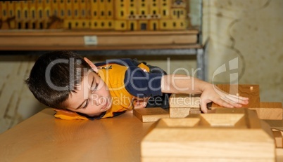 Cute little boy plays with wooden bricks indoors and builds a house