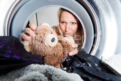 junge Frau holt nassen Teddybär aus einer Waschmaschine