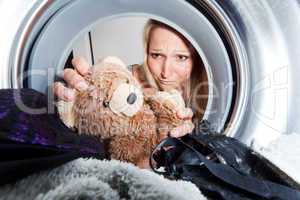 junge Frau holt nassen Teddybär aus einer Waschmaschine