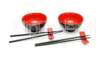 Two sets of chopsticks on stands anongside the red and black Japanese bowls