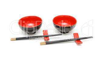 Two sets of chopsticks on stand anongside the red and black Japanese bowls