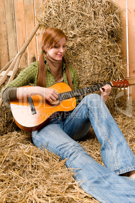 Young country woman playing guitar in barn