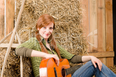 Young country woman playing guitar in barn