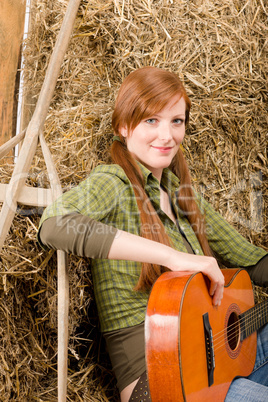 Young country woman playing guitar in barn