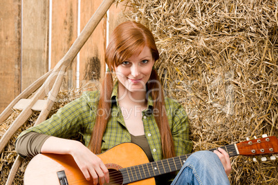Young country woman playing guitar in barn