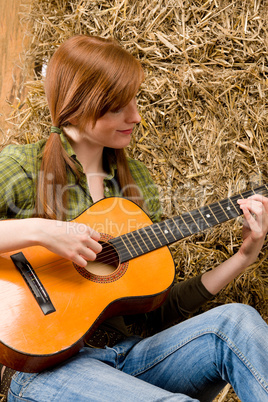 Young country woman playing guitar in barn