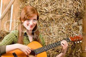 Young country woman playing guitar in barn