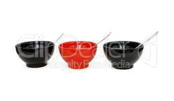 Row of two black and one red porcelain bowls with spoons isolated