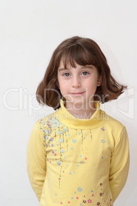 Serious cute little girl stands against the wall