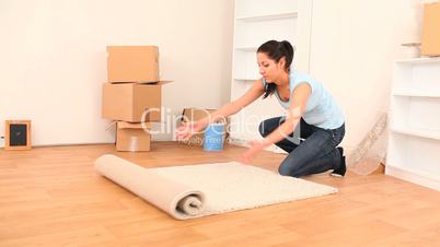 junge Frau rollt Teppich in ihrer neuen Wohnung aus
