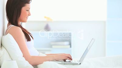 junge Frau sitzt mit Laptop im Bett