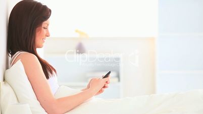 junge Frau sitzt mit Handy im Bett