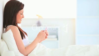 junge Frau sitzt mit Handy im Bett