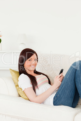 Attractive red-haired woman writing a text on her phone while ly