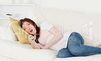 Attractive red-haired woman watching tv while lying on a sofa