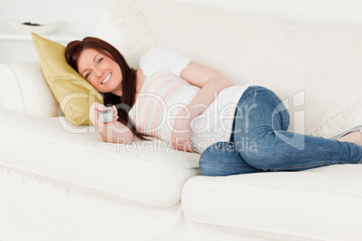 Beautiful red-haired woman watching tv while lying on a sofa