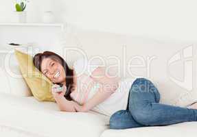 Good looking red-haired woman watching tv while lying on a sofa