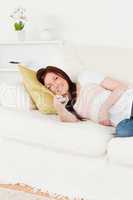 Pretty red-haired woman watching tv while lying on a sofa