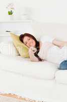 Cute red-haired woman watching tv while lying on a sofa