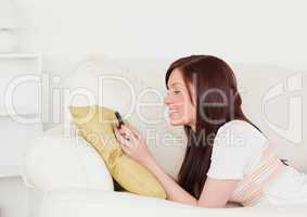 Pretty red-haired female writing a text on her phone while lying