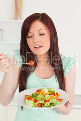 Pretty red-haired woman enjoying a mixed salad in the kitchen