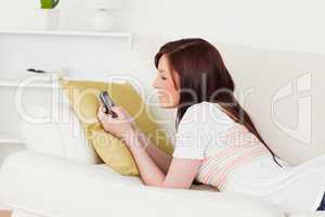 Charming red-haired female writing a text on her phone while lyi